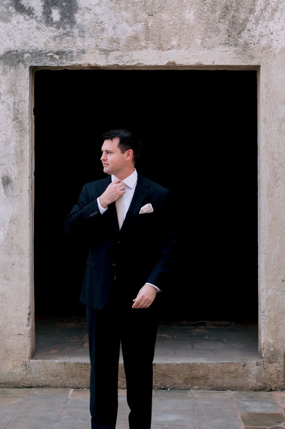 Groom adjusts his tie inside a stone doorway at Santa Clara Ruins, Antigua Guatemala.