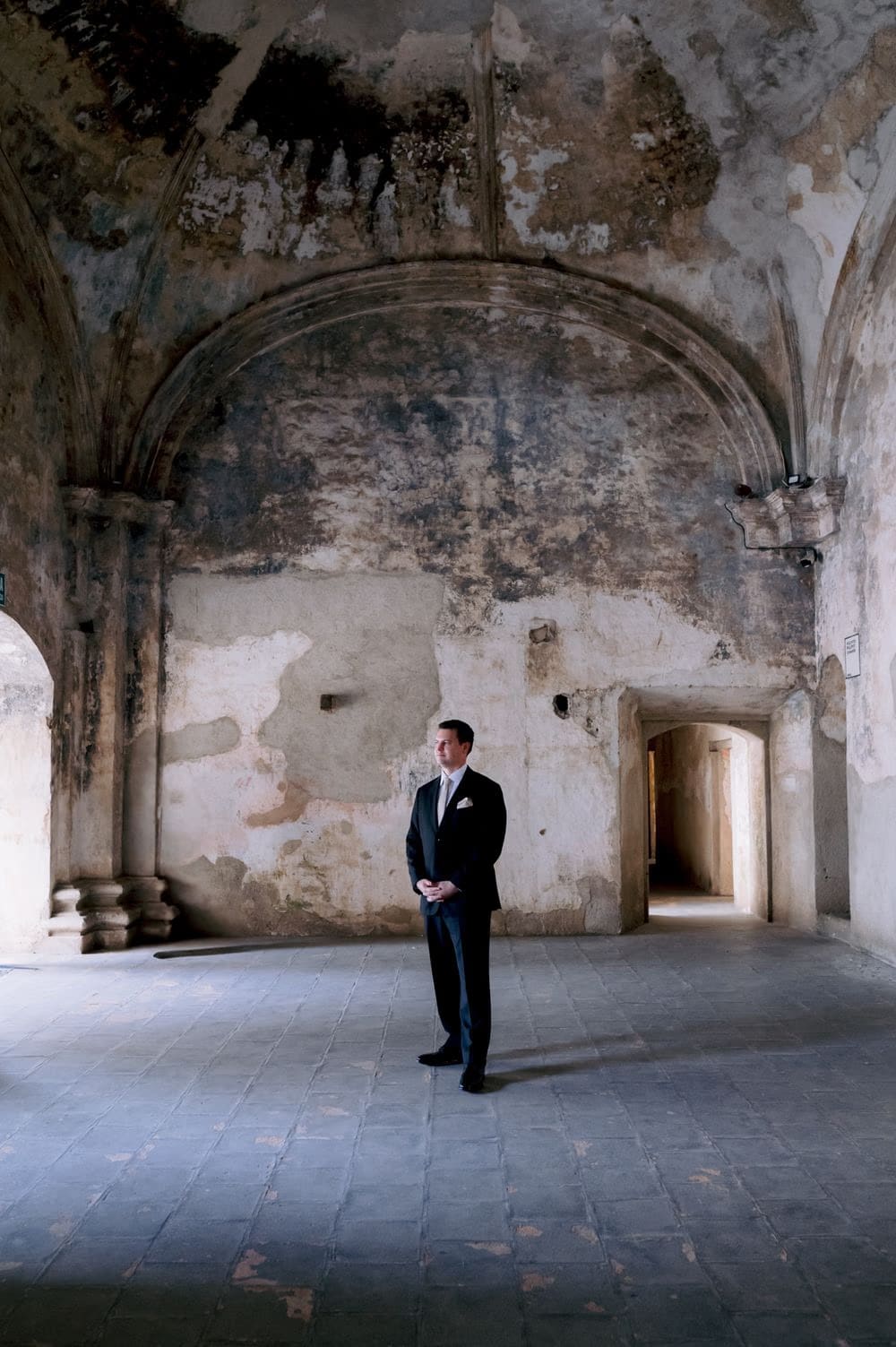 Groom Nathan stands beneath a soaring vaulted ceiling at Santa Clara Ruins before his Antigua Guatemala wedding.