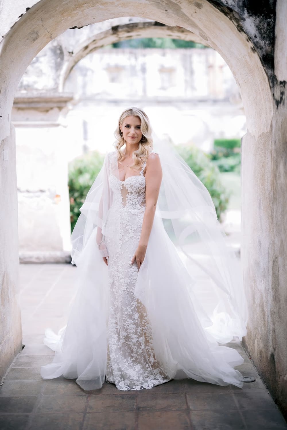 Bride framed by a stone arch with veil and lace gown flowing — bridal portrait at Santa Clara Ruins.