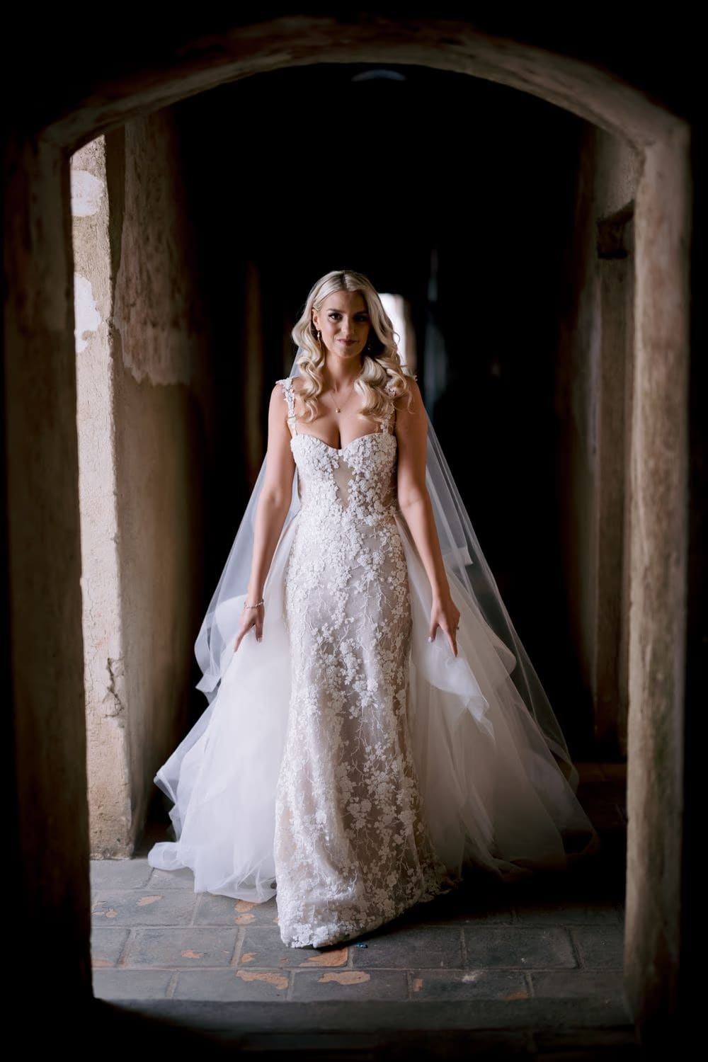 Bride walks through a stone arch of Santa Clara Ruins toward the camera — destination wedding portrait in Antigua Guatemala.