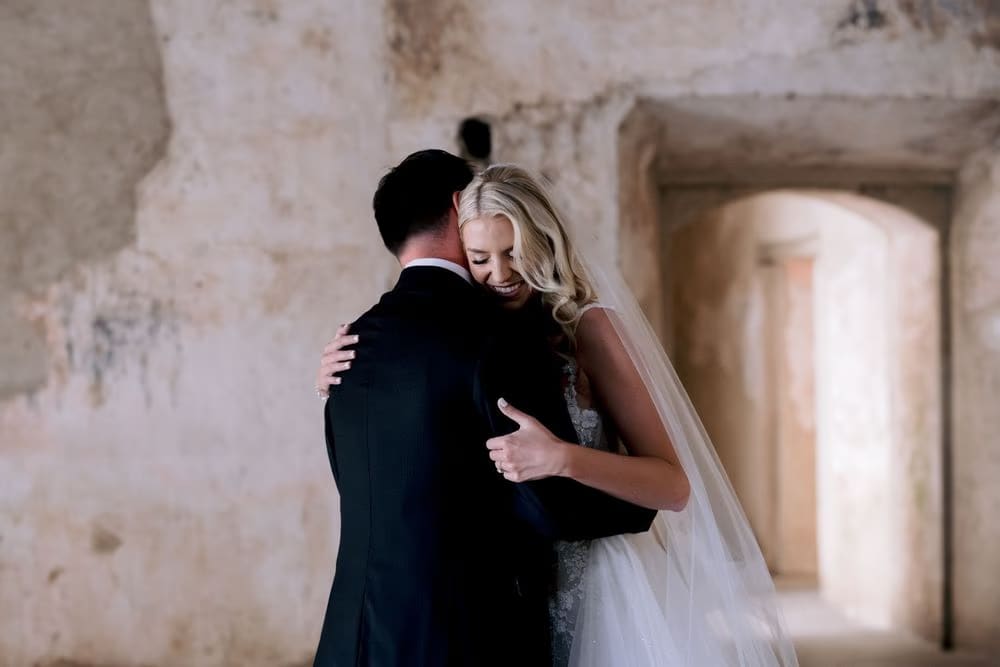 Bride rests her head on her groom's shoulder beneath the arches of Santa Clara during the first look.