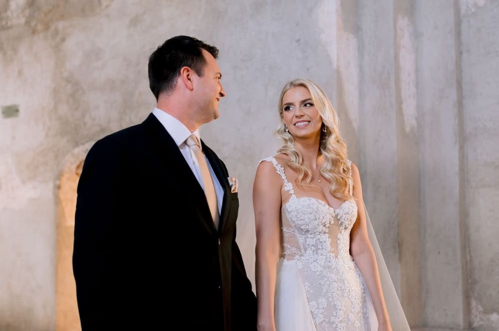 Bride laughs with her groom against a sunlit ruin wall at Santa Clara — editorial couple portrait.