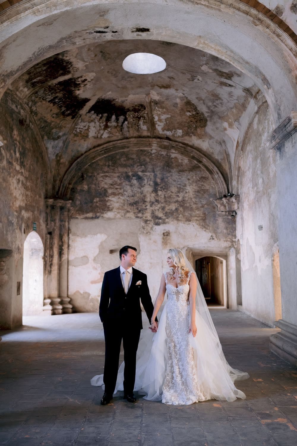 Sydney and Nathan hold hands beneath the painted vault of Santa Clara Ruins in colonial Antigua.
