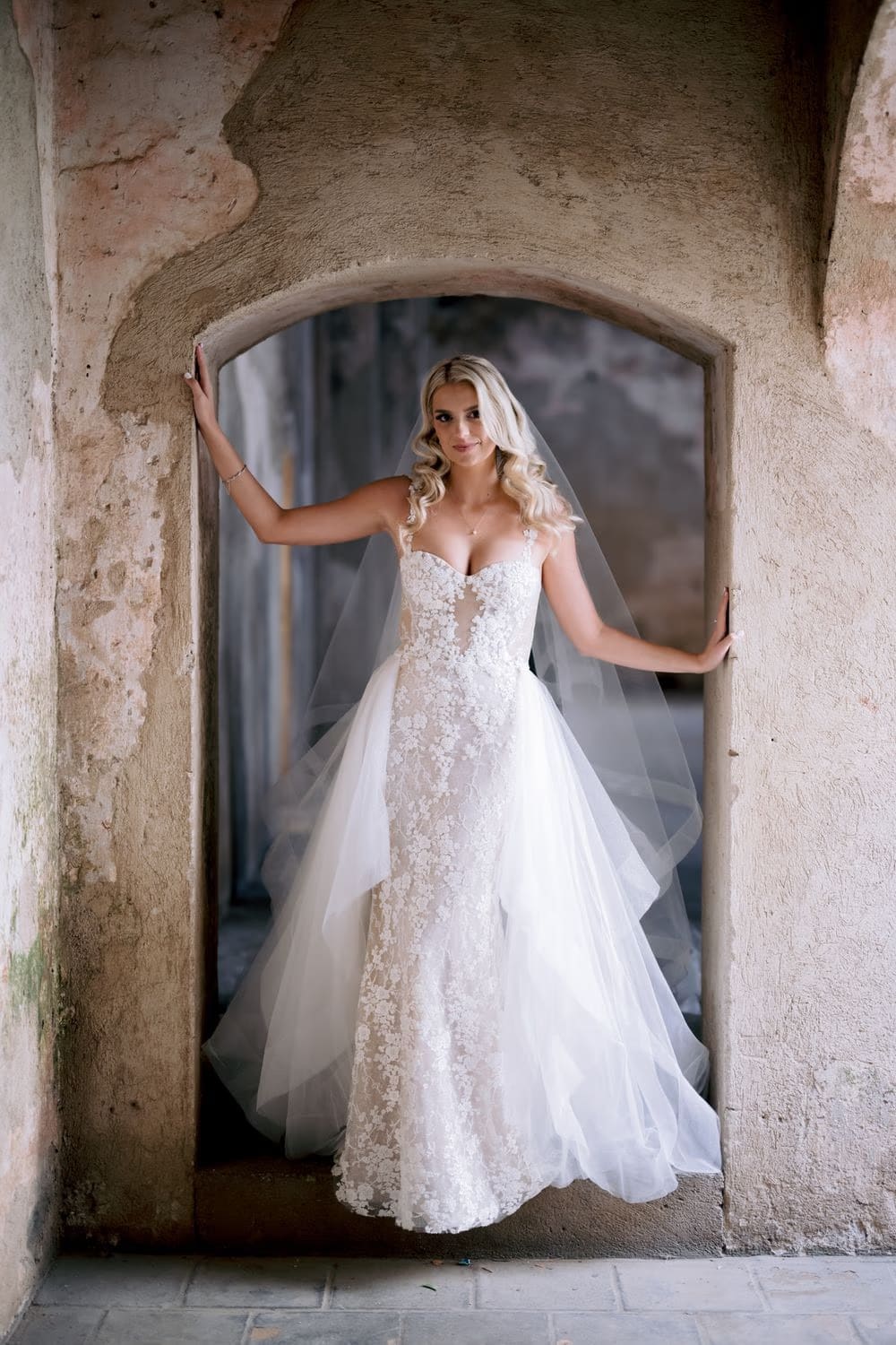 Bride frames herself with both hands in a Santa Clara arched doorway — destination bridal portrait.