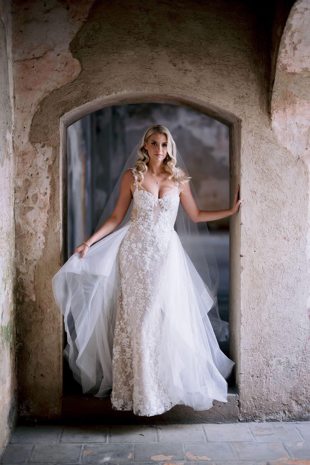 Bride sways her gown inside a Santa Clara arched doorway with her veil catching the breeze.
