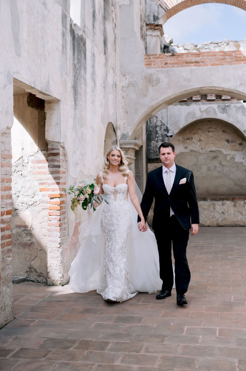 Sydney and Nathan walk hand in hand past the brick arches of La Recolección Ruins in Antigua Guatemala.