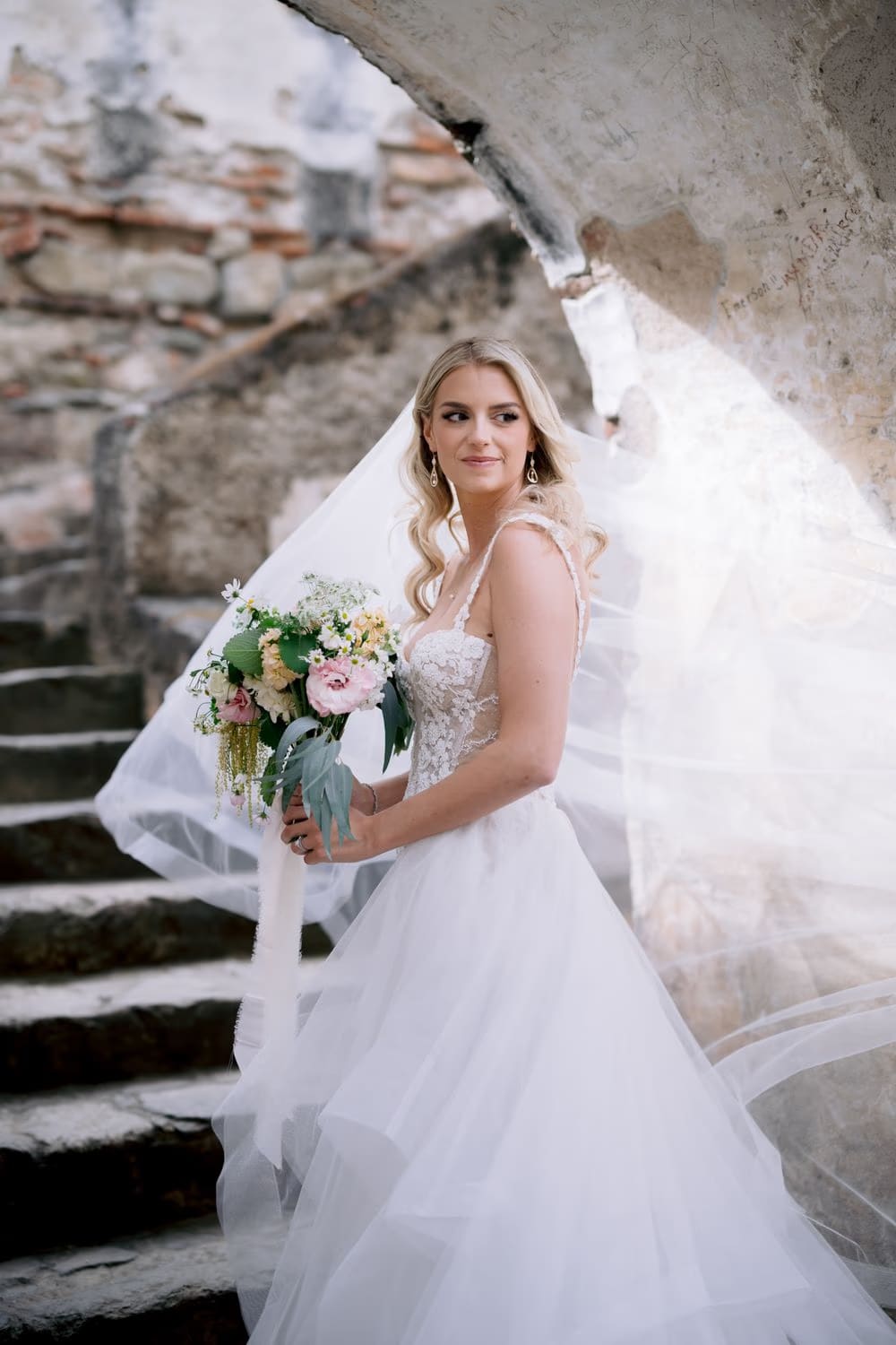 Bride glances over her shoulder on the stone staircase of La Recolección Ruins, veil mid-swing.