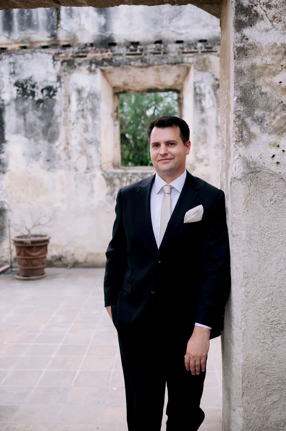 Groom Nathan leans against a weathered ruin wall in colonial Antigua — editorial groom portrait.