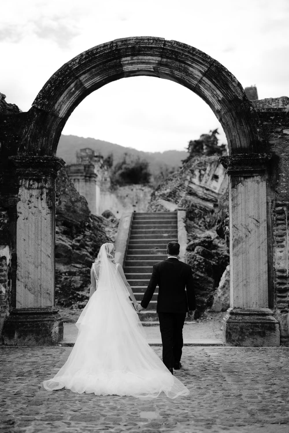 Sydney, Nathan and their wedding party gather on the stone staircase amid La Recolección Ruins in Antigua Guatemala.