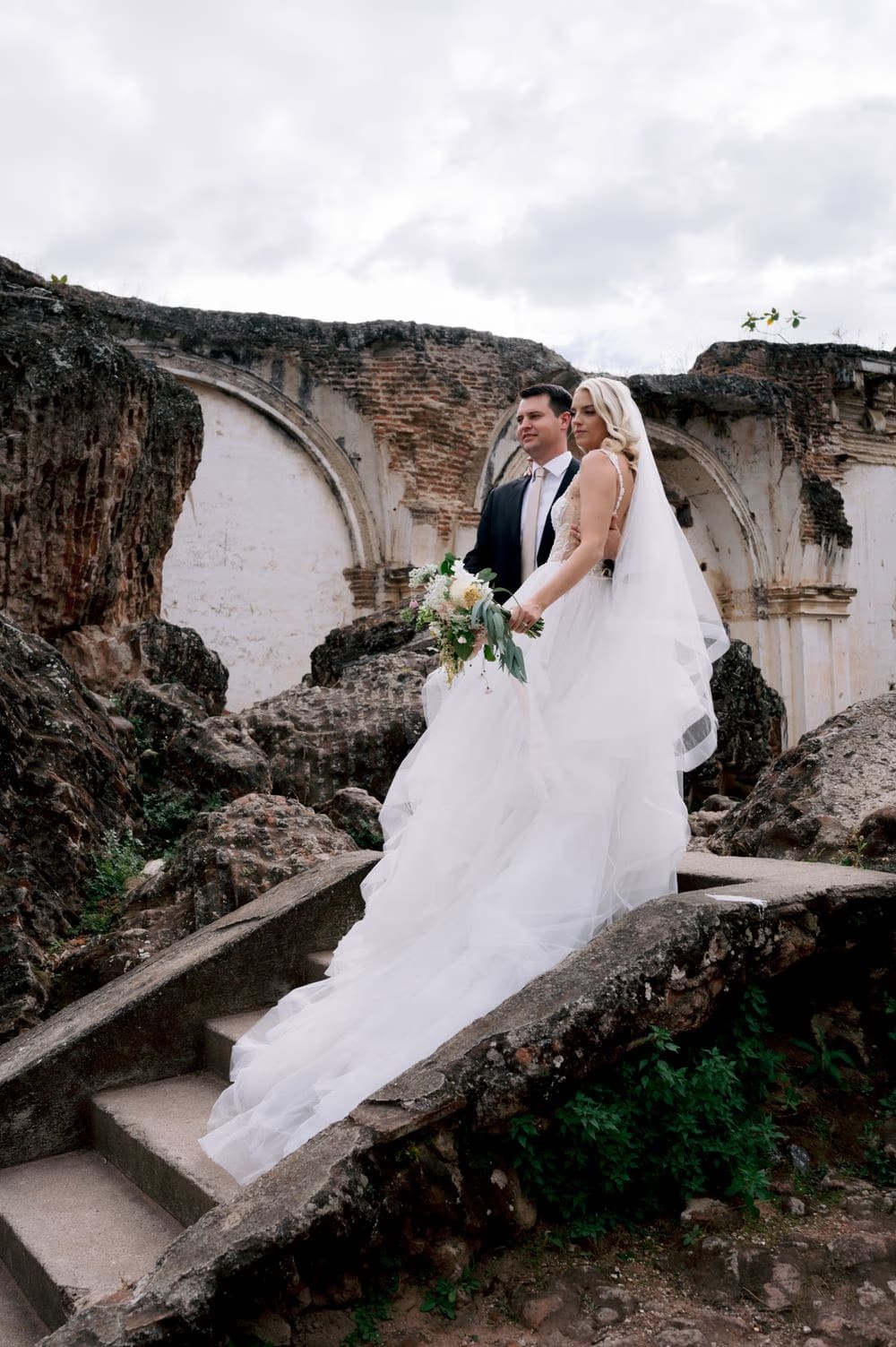Bride and groom descend a stone path through La Recolección Ruins after their portraits in Antigua Guatemala.