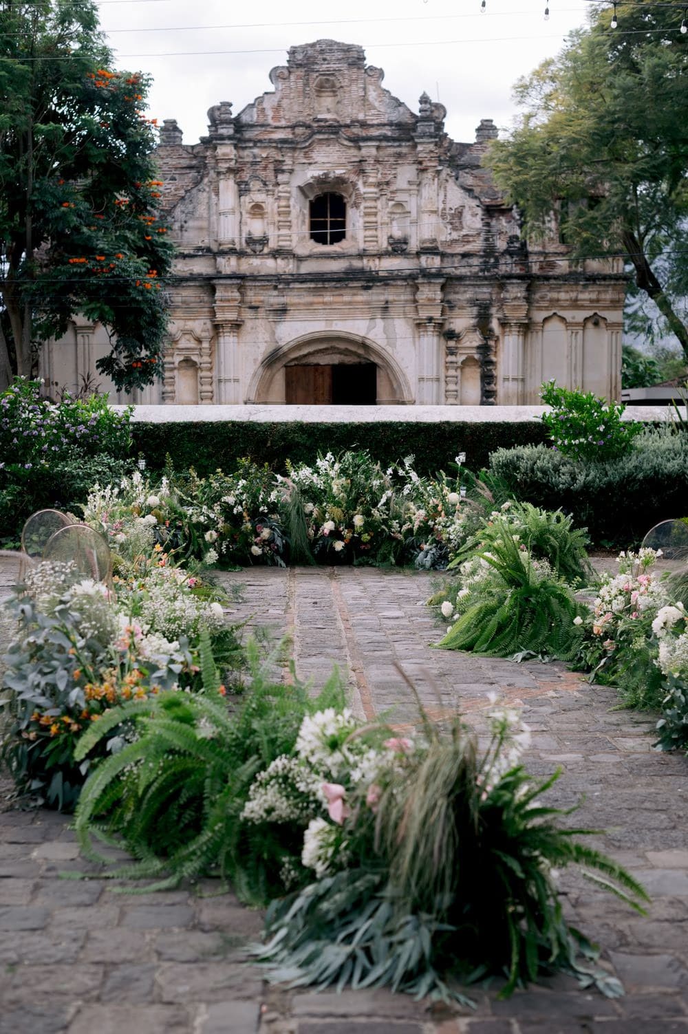 Garden ceremony aisle set with ferns, wildflowers and ghost chairs facing the San José el Viejo facade in La Antigua.