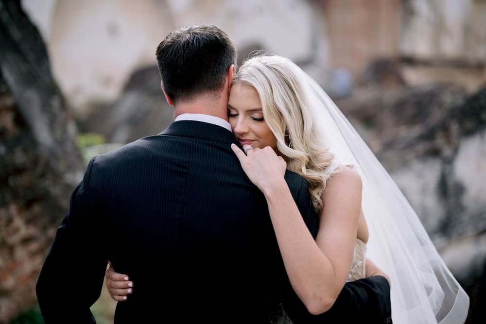 Bride closes her eyes against her groom's shoulder in a quiet moment among the ruins of La Recolección.