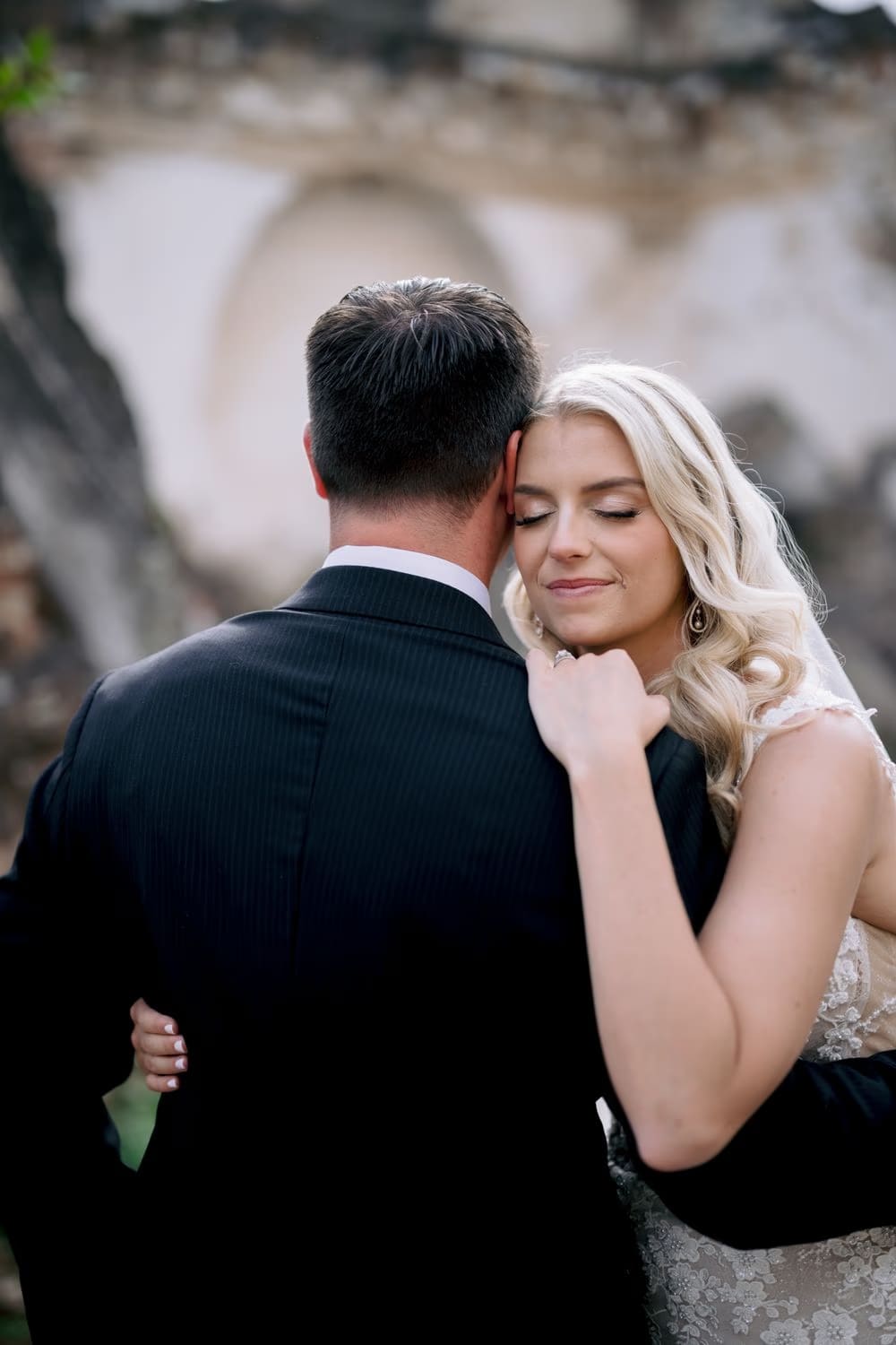 Bride and groom rest cheek to cheek with a domed ruin arch in soft focus behind them.