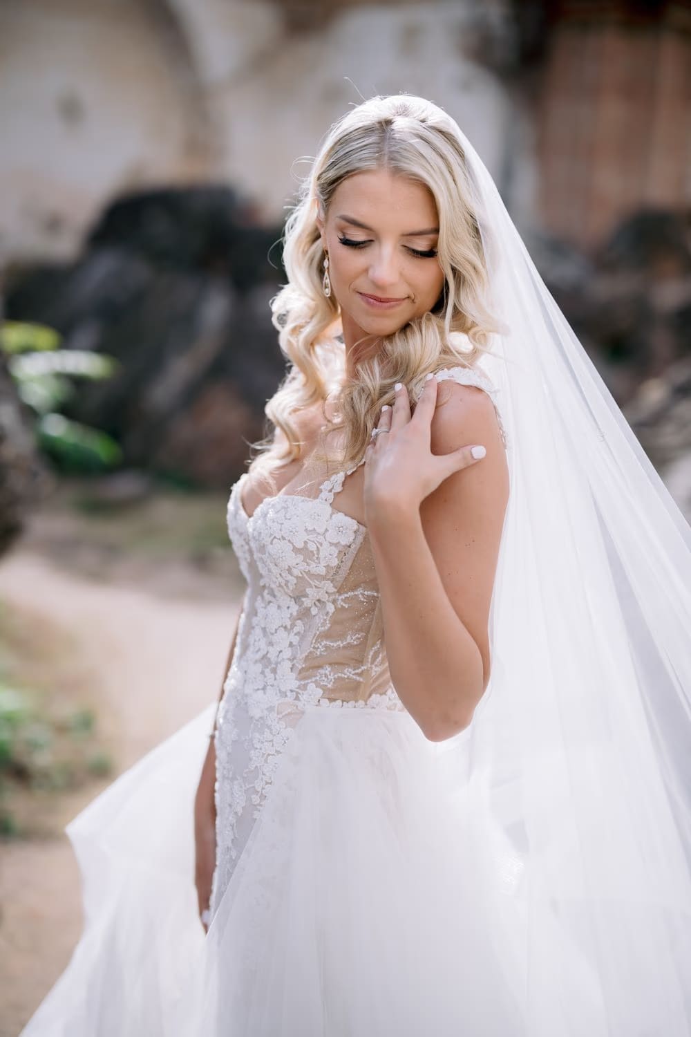 Close-up bridal portrait of Sydney looking down with her hand resting near her shoulder strap.
