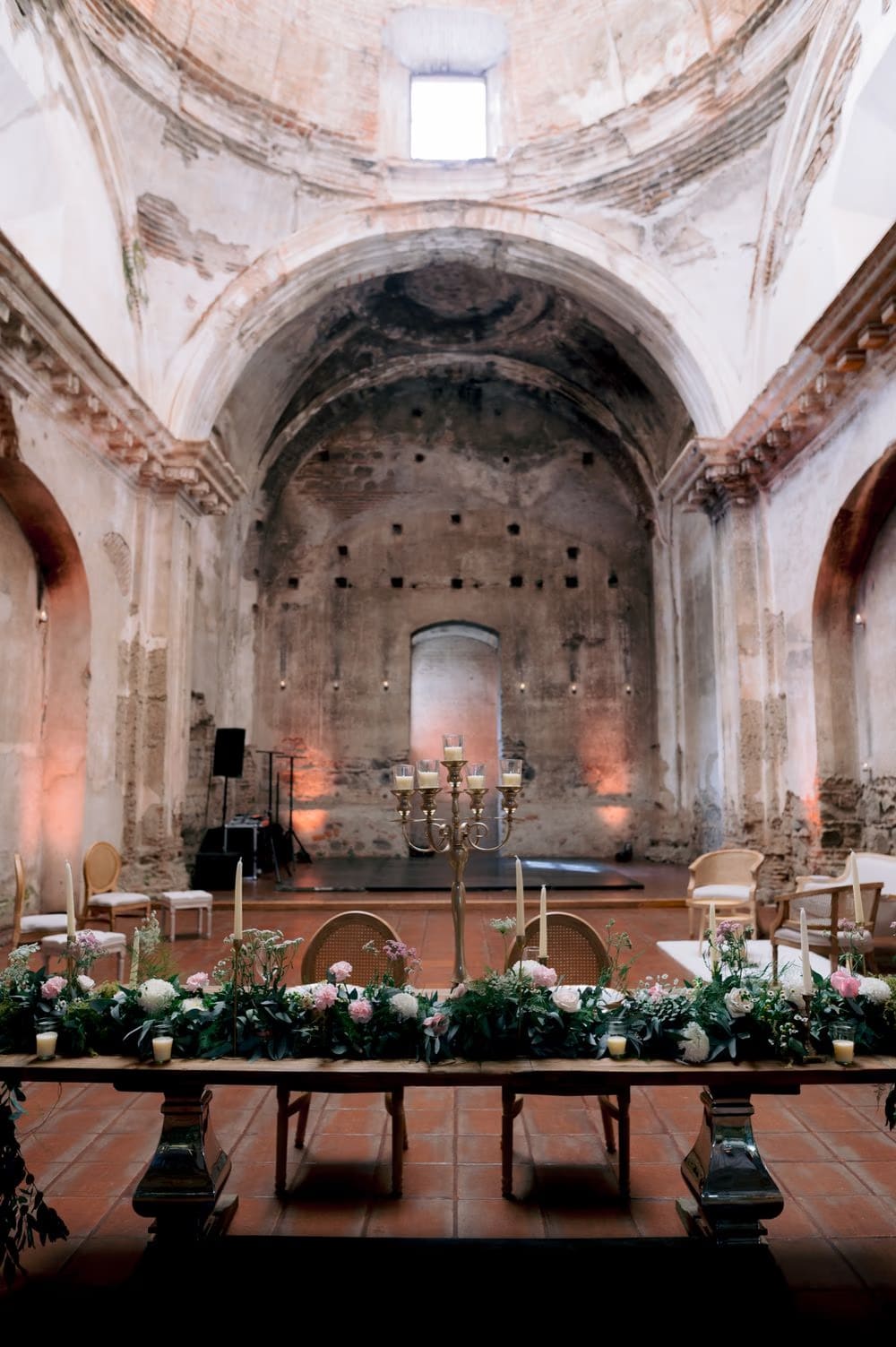 Long candlelit reception table set inside the nave of San José el Viejo Ruins, garlands trailing across the wood.