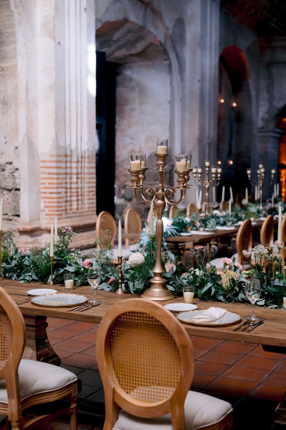 Brass candelabra centerpiece surrounded by greenery garland and rose-pink florals at the San José el Viejo reception.