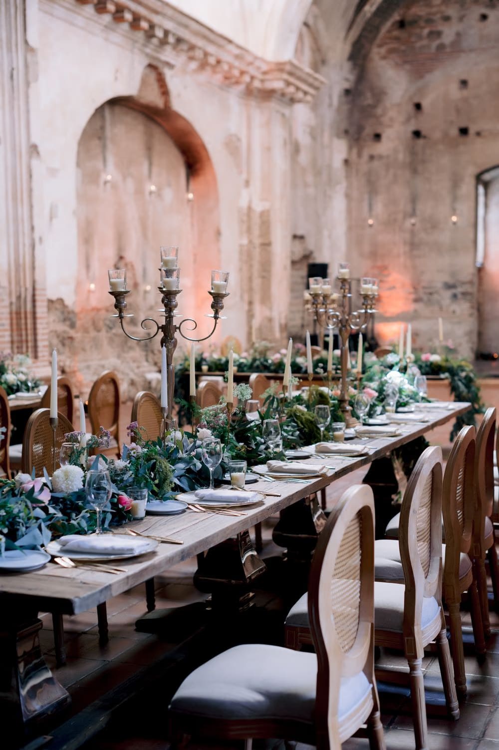 Reception tablescape with silver candelabras, taper candles and trailing greenery inside the ruin nave at San José el Viejo.
