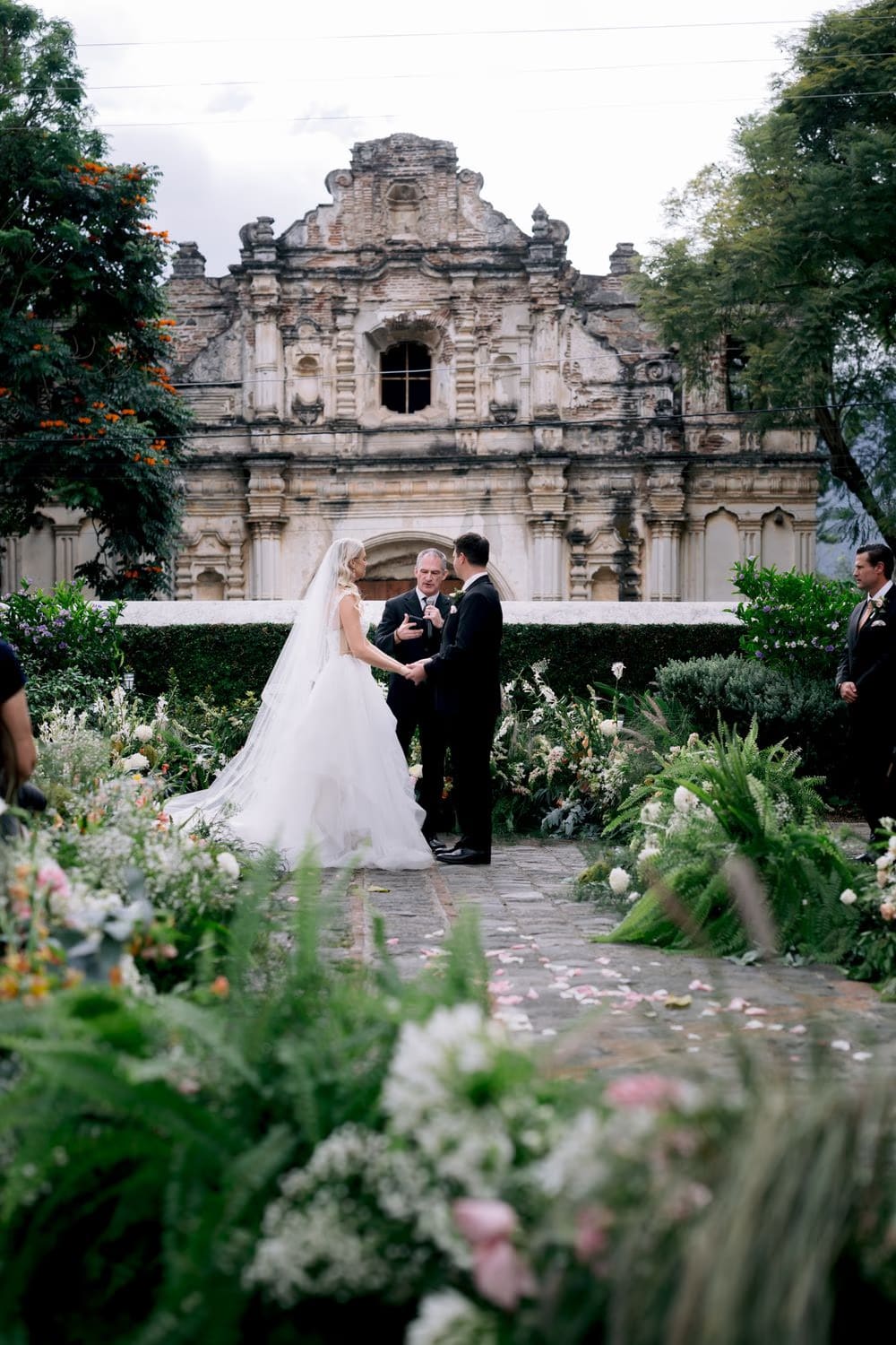 Wedding ceremony moment framed by lush greenery and wildflowers in front of the San José el Viejo facade.