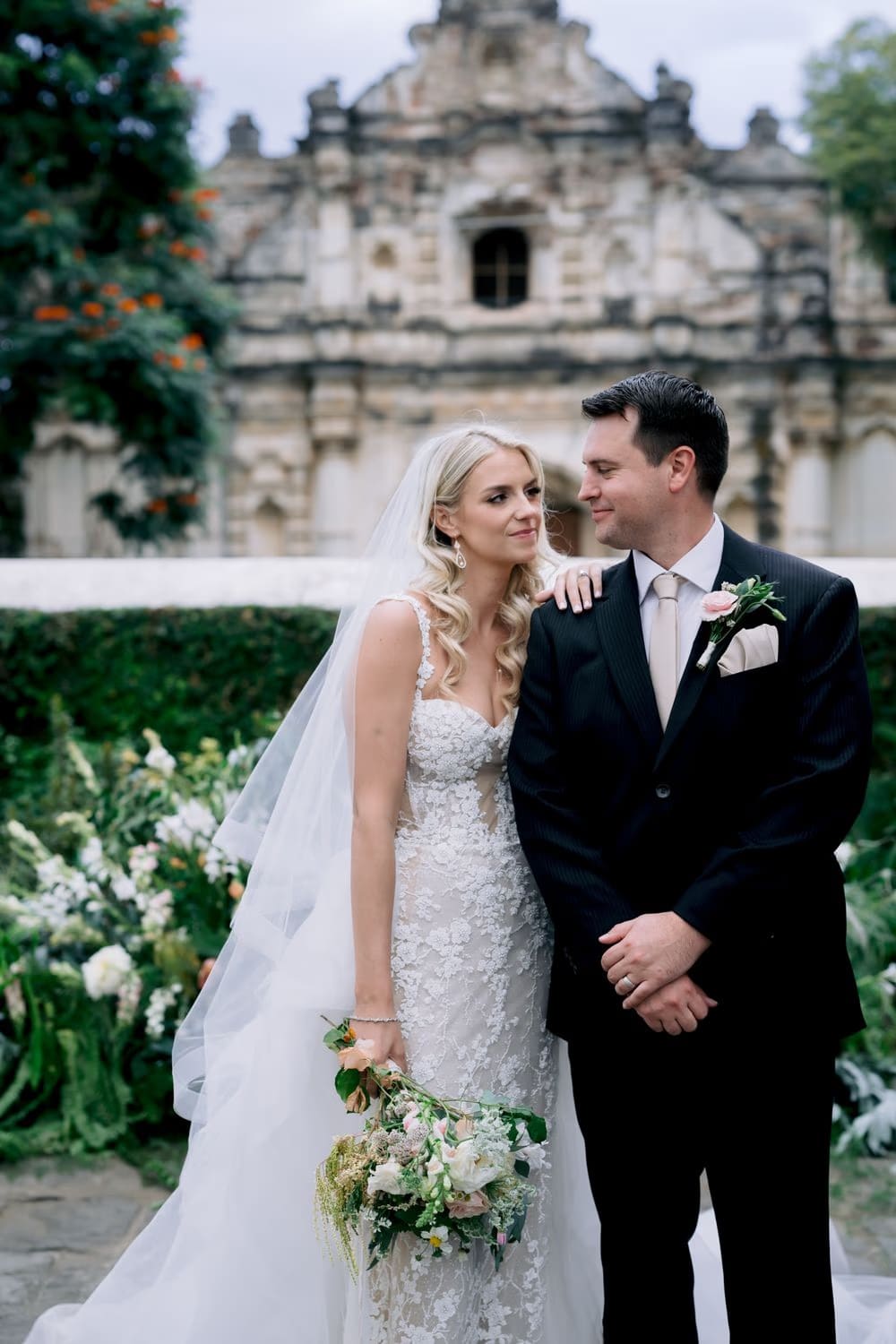 Bride and groom look out together with the San José el Viejo facade rising behind them — destination wedding portrait.