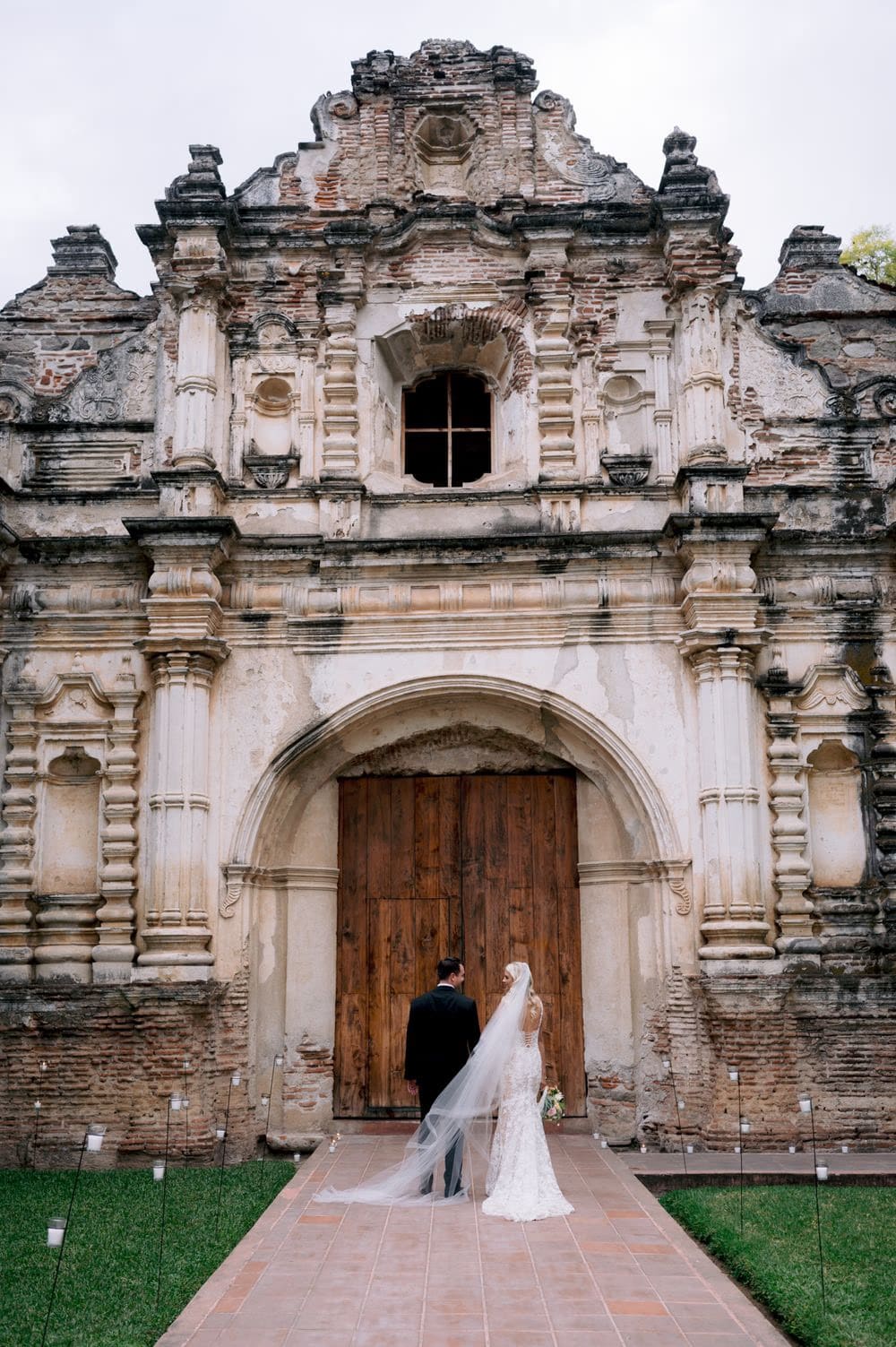 Bride and groom walk toward the towering wooden doors of San José el Viejo Ruins after their ceremony.