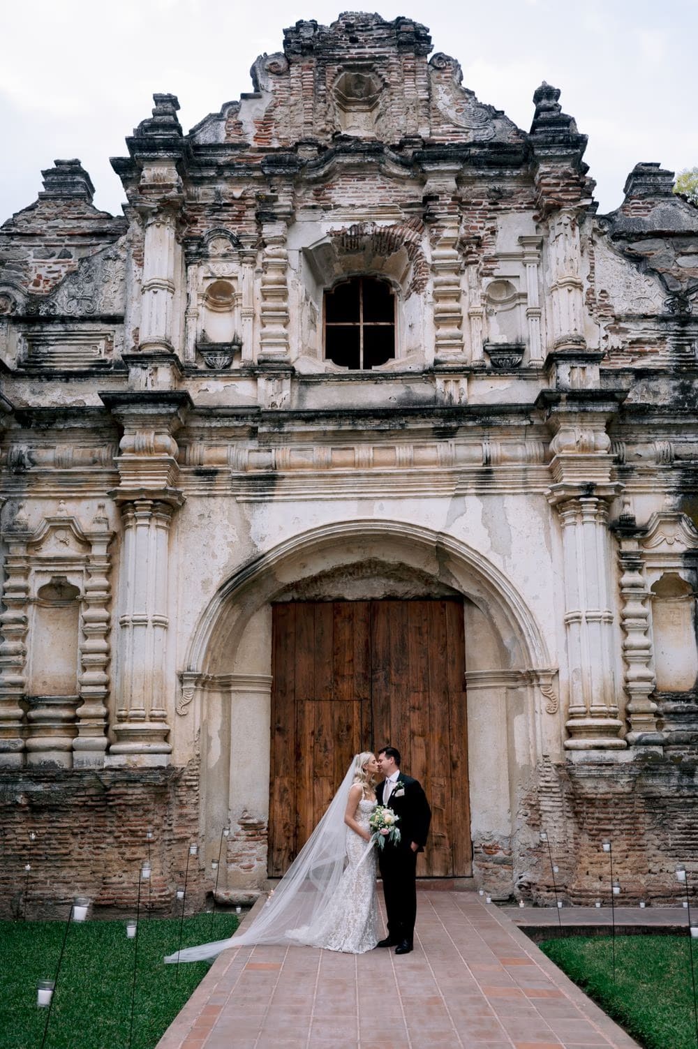 Bride and groom share a soft kiss in front of the carved baroque facade of San José el Viejo in Antigua Guatemala.