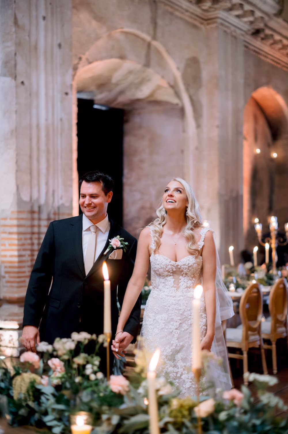 Sydney looks up in wonder at the ruin's vaulted ceiling as Nathan smiles beside her at the reception.