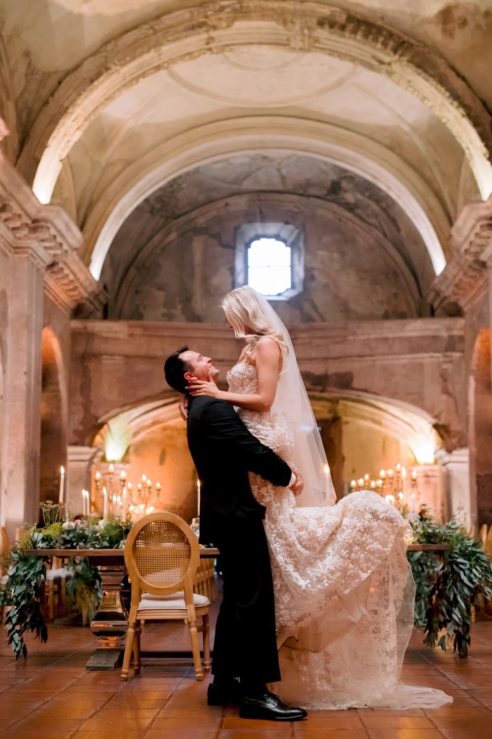 Groom lifts the bride in the air beneath the vaulted ceiling of San José el Viejo during their reception.