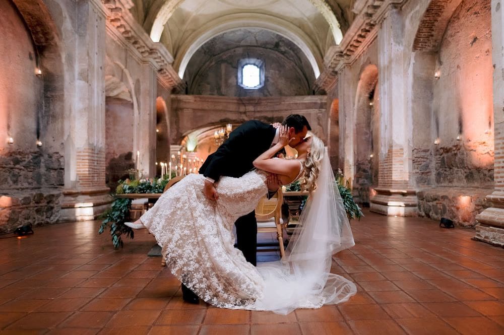 Groom dips his bride for a kiss between the candle-lit reception tables at San José el Viejo.