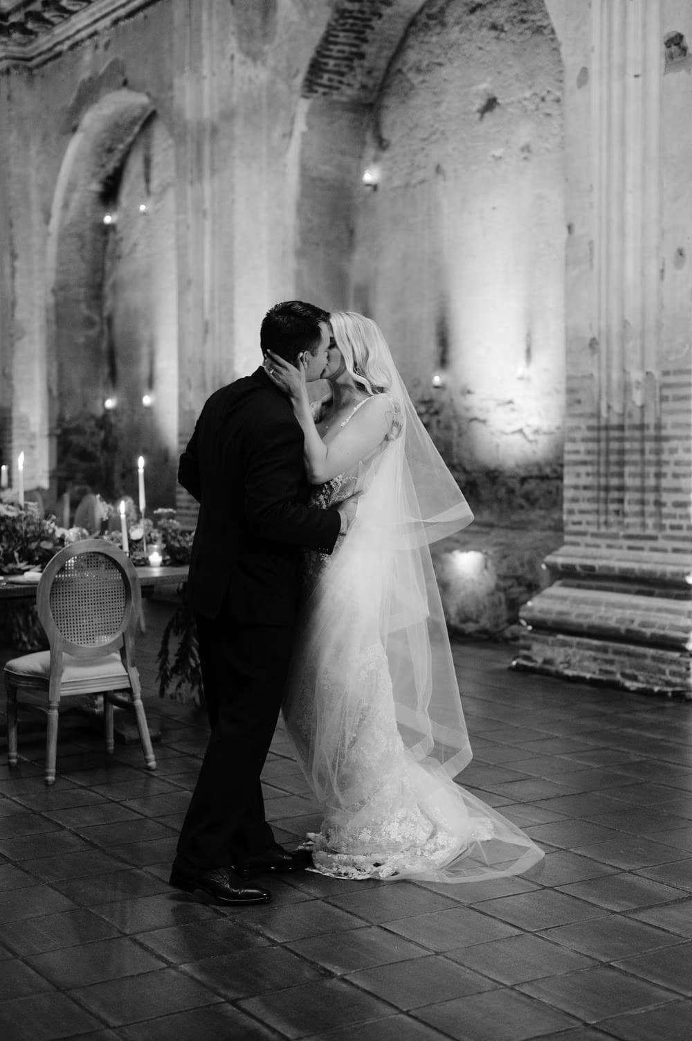 Black-and-white kiss between bride and groom inside the candle-lit nave of San José el Viejo Ruins.