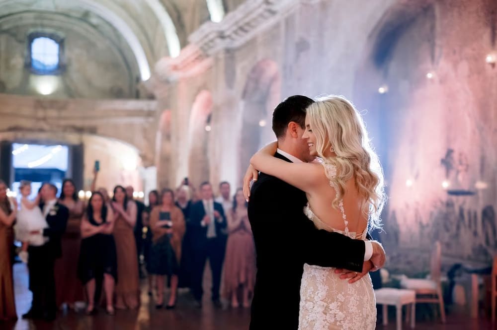 Bride and groom hold each other close during their first dance with guests watching at the San José el Viejo reception.