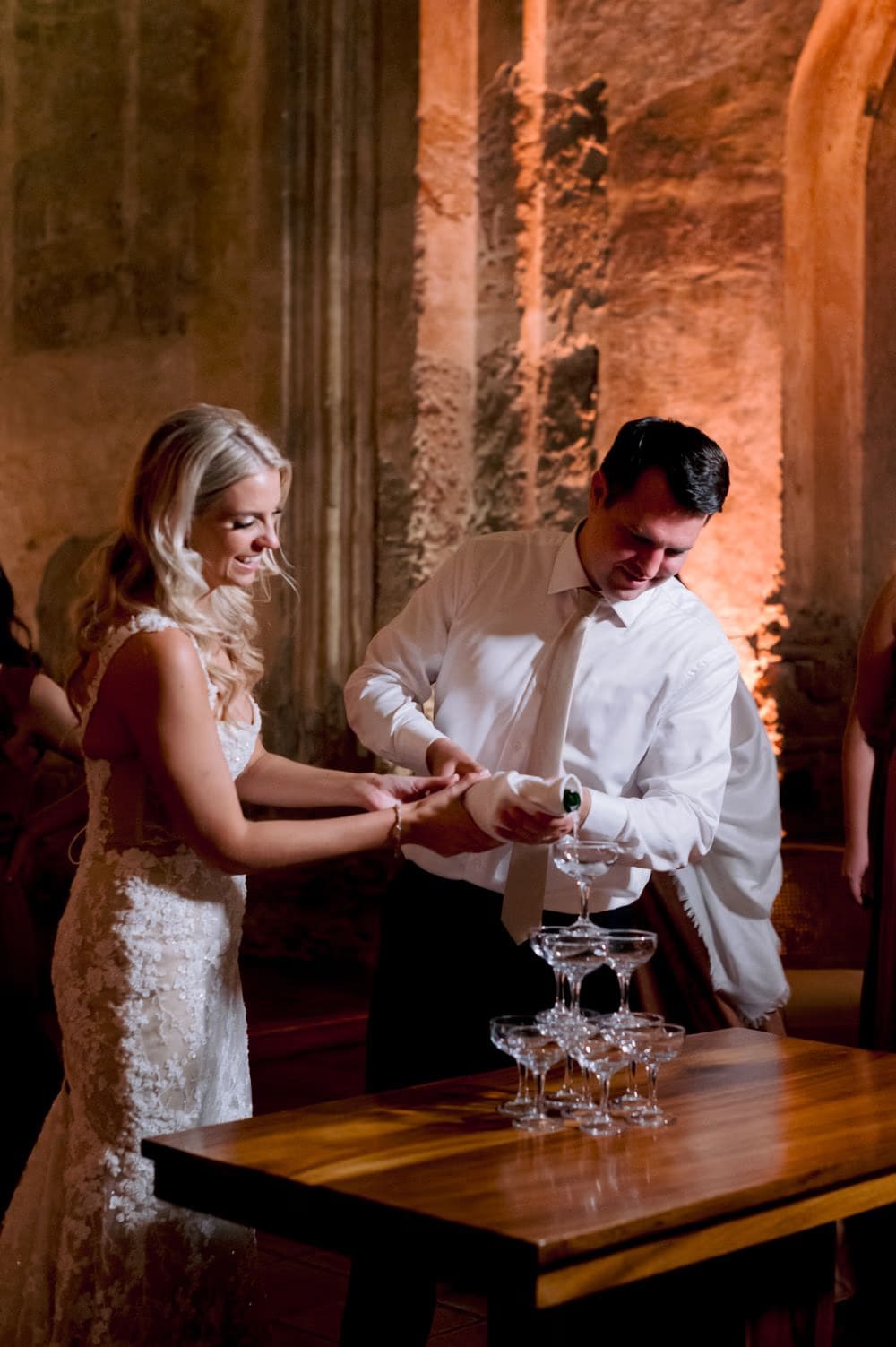 Sydney and Nathan pour a champagne tower during the reception inside the candle-lit nave of San José el Viejo.