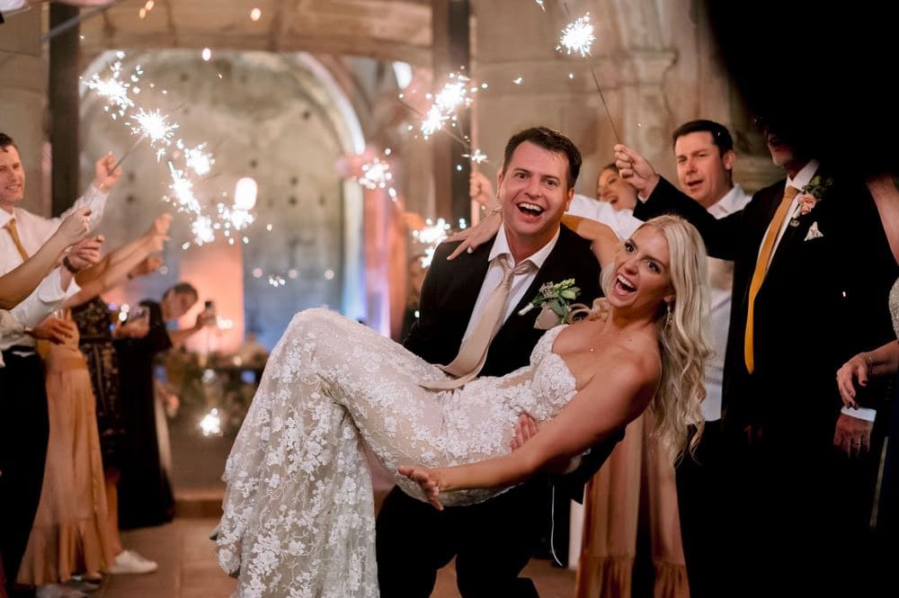 Groom carries the bride in his arms through the sparkler tunnel of guests at the San José el Viejo reception.