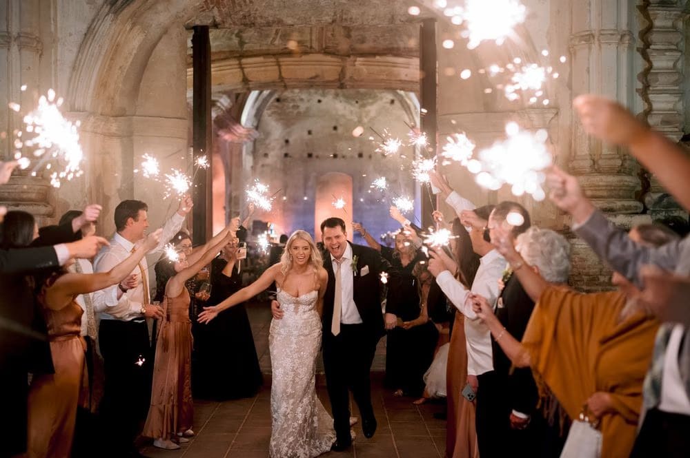 Sydney and Nathan run hand in hand through a tunnel of sparklers held by guests, closing their San José el Viejo wedding night.