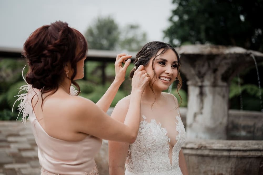 Bridesmaid adjusts the bride's hair beside a colonial stone fountain in Antigua Guatemala.