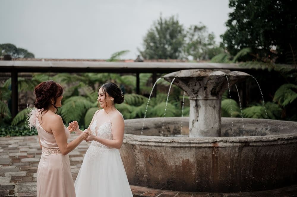 Bride and bridesmaid laugh by a fern-framed stone fountain at Hotel Casa Santo Domingo.