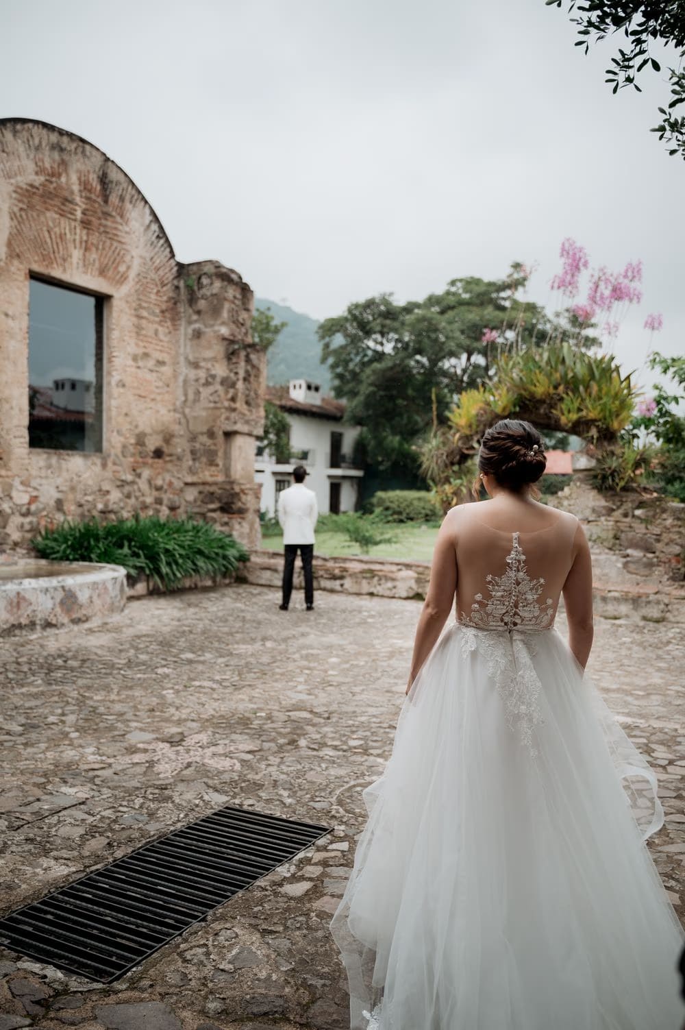 First-look moment as the bride approaches the groom across the cobblestones with Volcán de Agua looming behind colonial ruins.