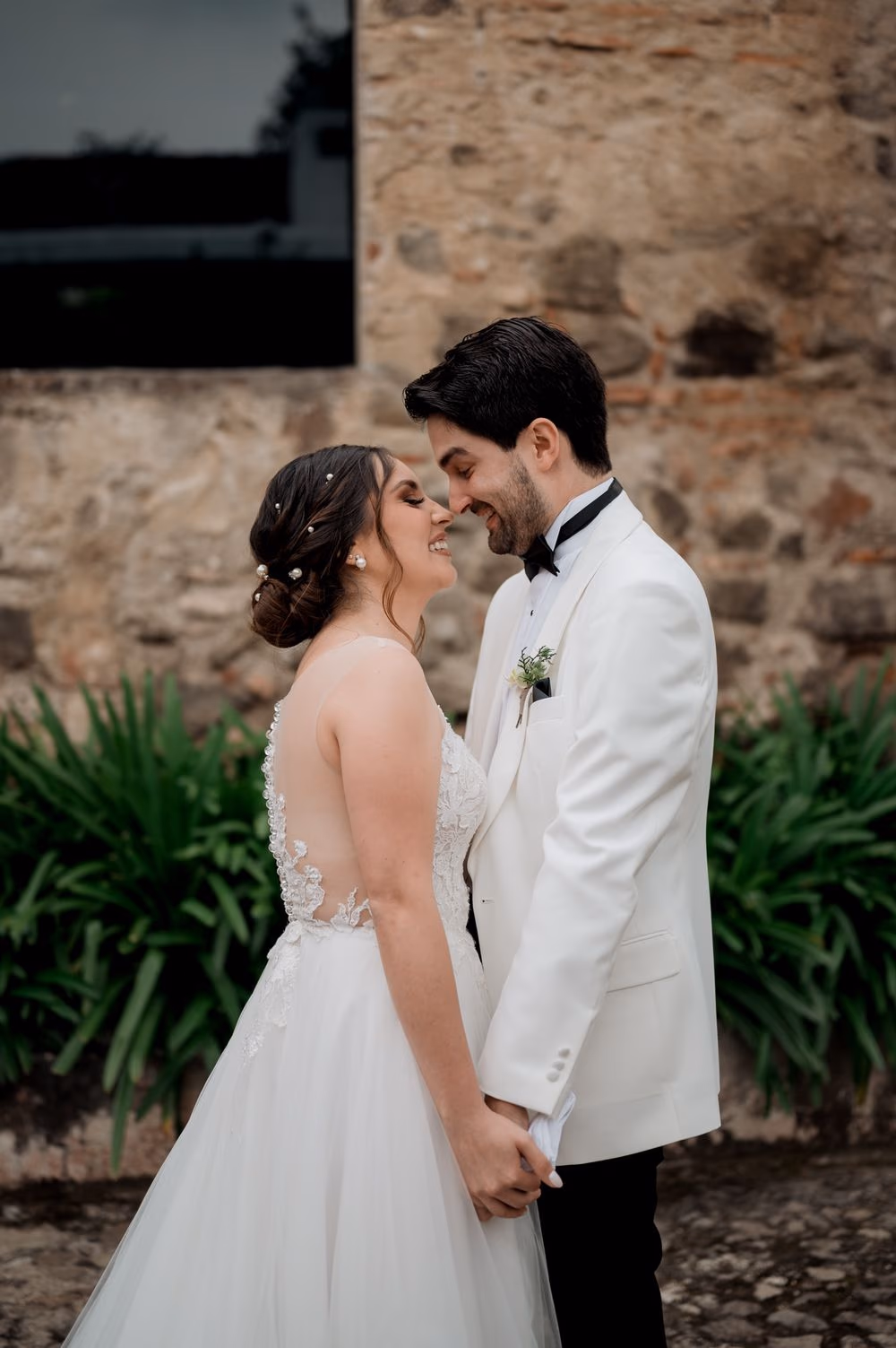 Vertical portrait of the couple foreheads touching with pearled bridal updo against a stone wall at Hotel Casa Santo Domingo.