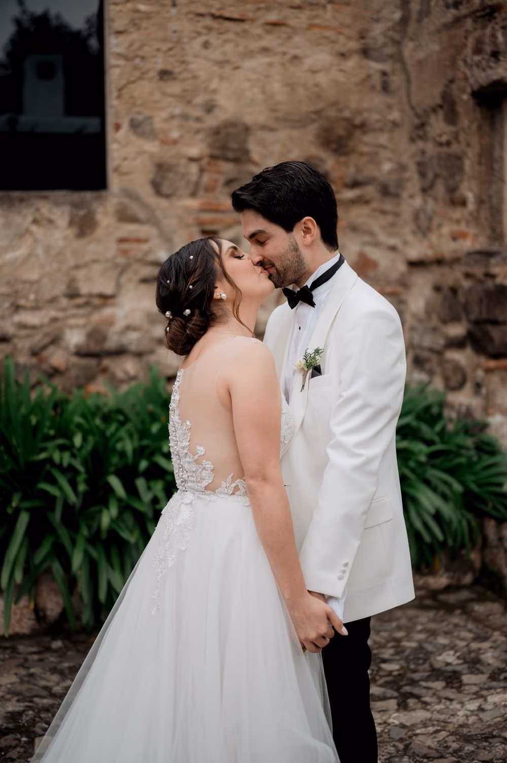 Bride and groom kiss after their first look against the rough stone monastery wall in Antigua Guatemala.