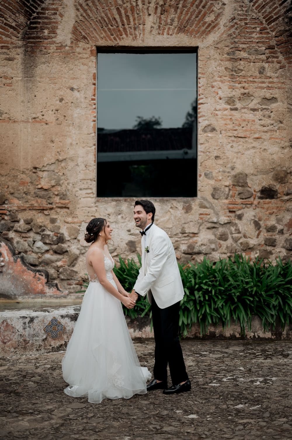 Couple hold hands and laugh in front of a tall ruined window arch at the monastery in Antigua Guatemala.