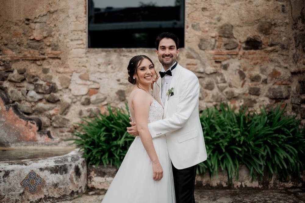 Couple embrace and smile during portraits in front of an old monastery wall at Casa Santo Domingo.