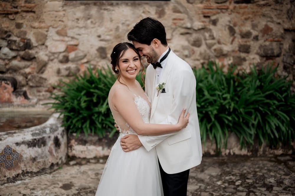 Bride laughs in the groom's arms against stone ruins and greenery — elegant wedding in Antigua Guatemala.