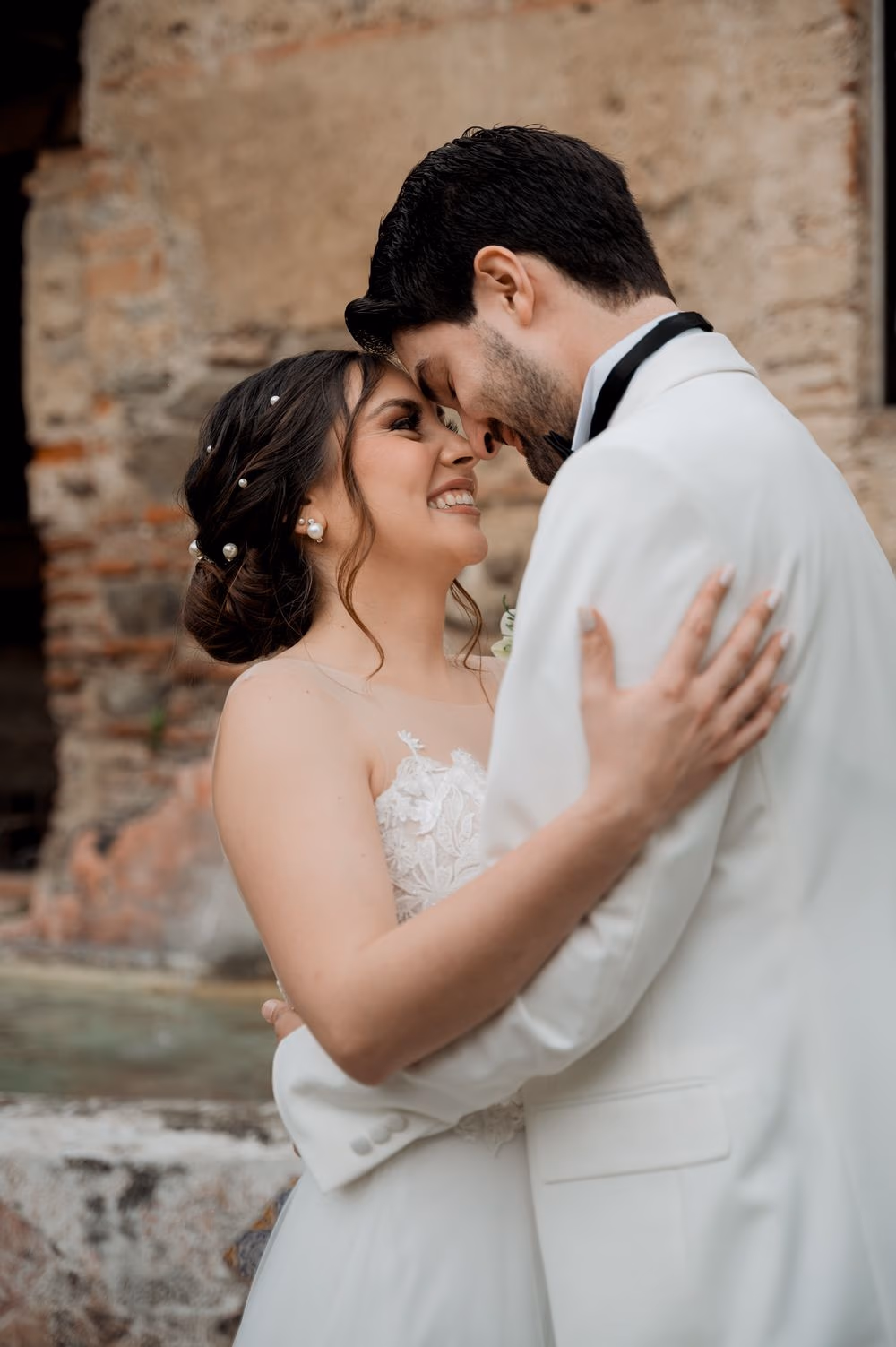 Intimate vertical portrait of the couple smiling forehead-to-forehead beside the stone fountain — Hotel Casa Santo Domingo.