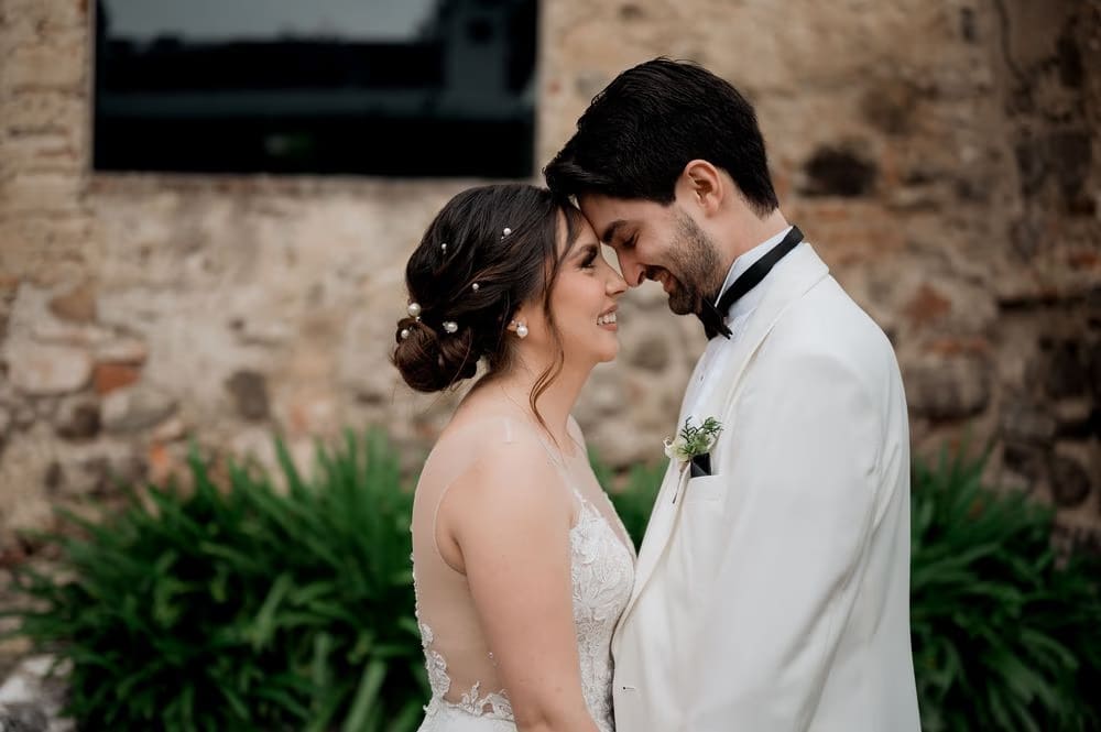 Profile portrait of the couple touching foreheads beside a fern wall at the colonial monastery.