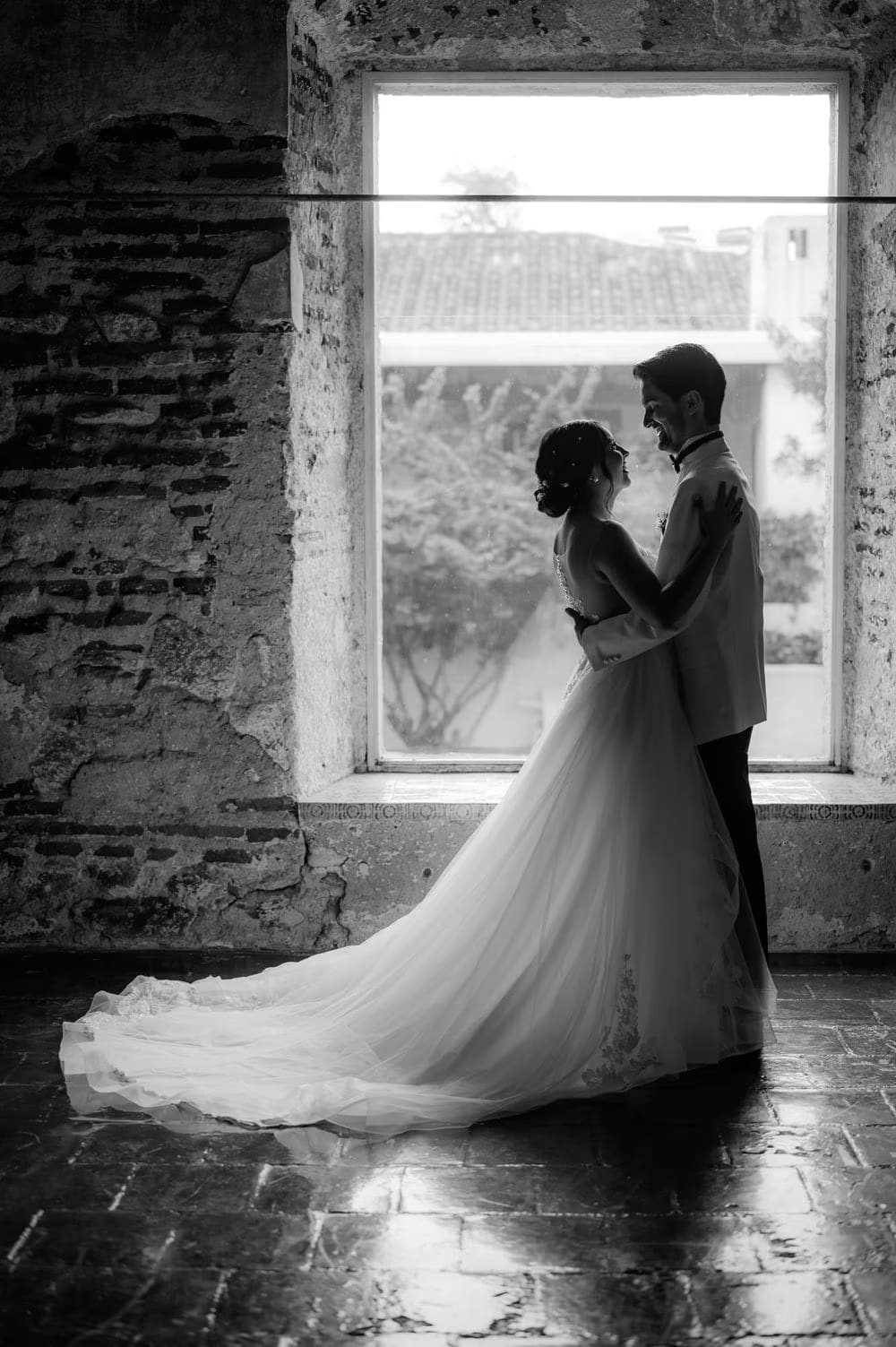 Black-and-white wide portrait of the couple holding each other in a stone window opening — colonial monastery in Antigua.
