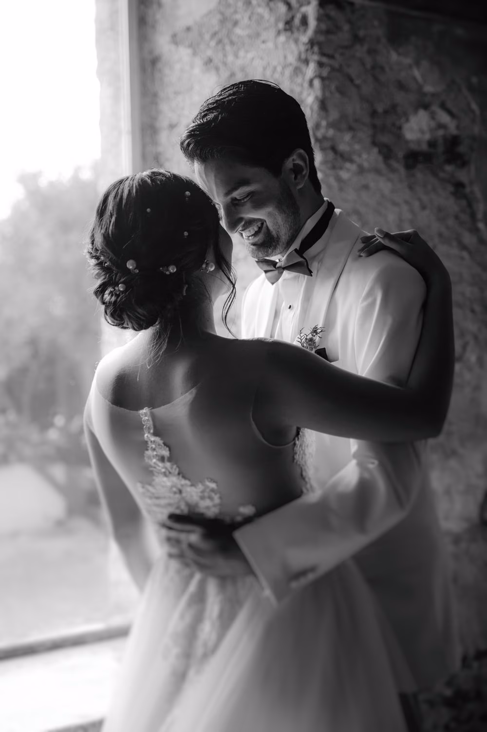 Soft black-and-white embrace of the couple beside an open window — editorial wedding portrait in Antigua.