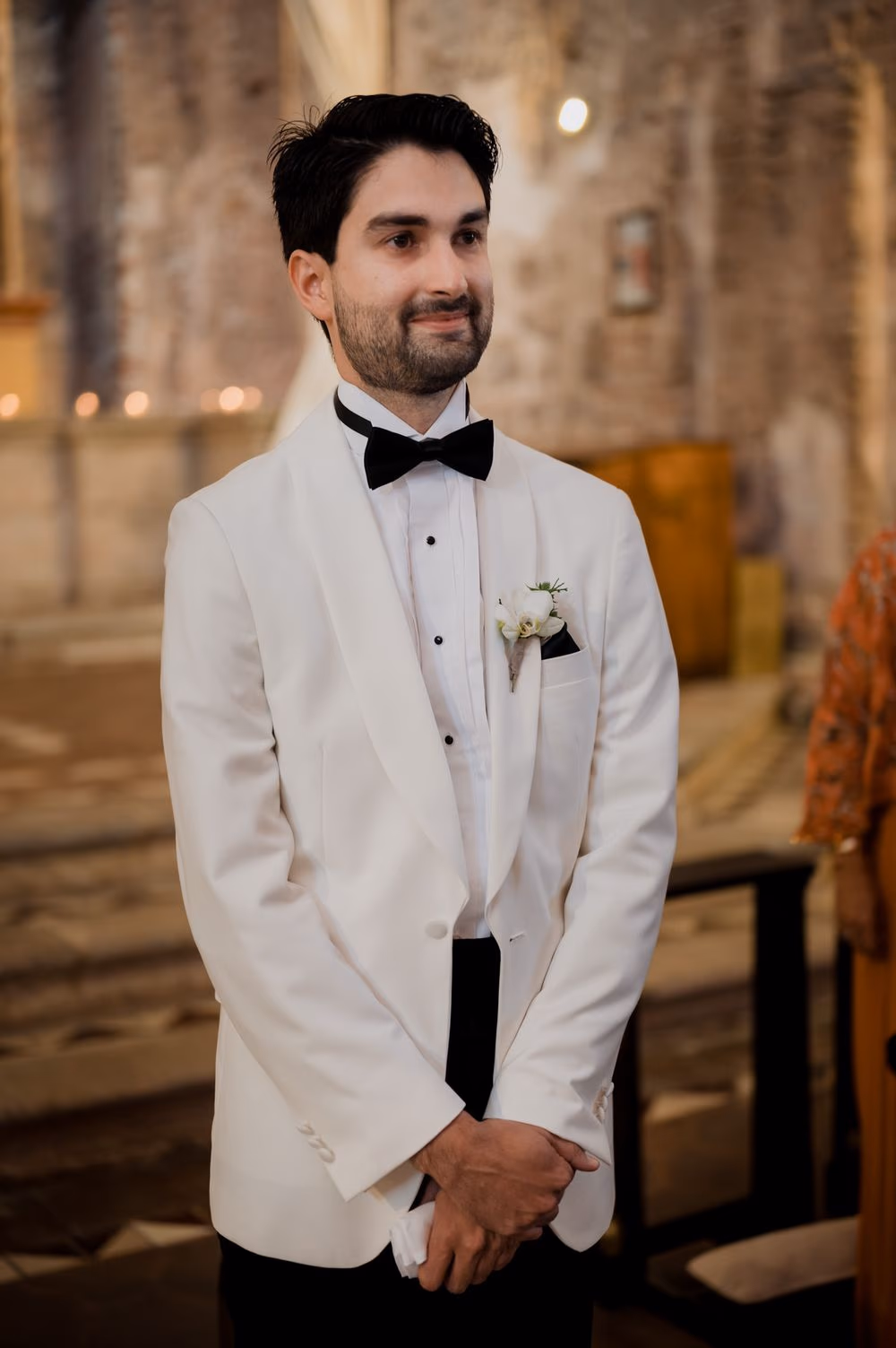 Ernesto waits at the altar in a white tuxedo as candles burn behind him during their wedding ceremony in Antigua Guatemala.