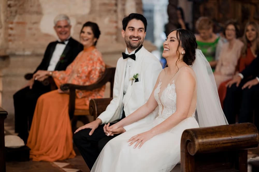 Couple laughing together during a light moment of the wedding ceremony with family in the background.