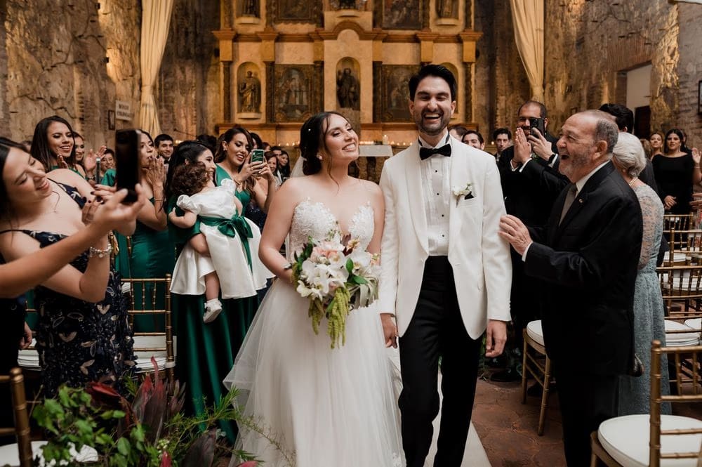 Newlyweds smile mid-aisle as guests cheer and applaud during the recessional at Casa Santo Domingo.