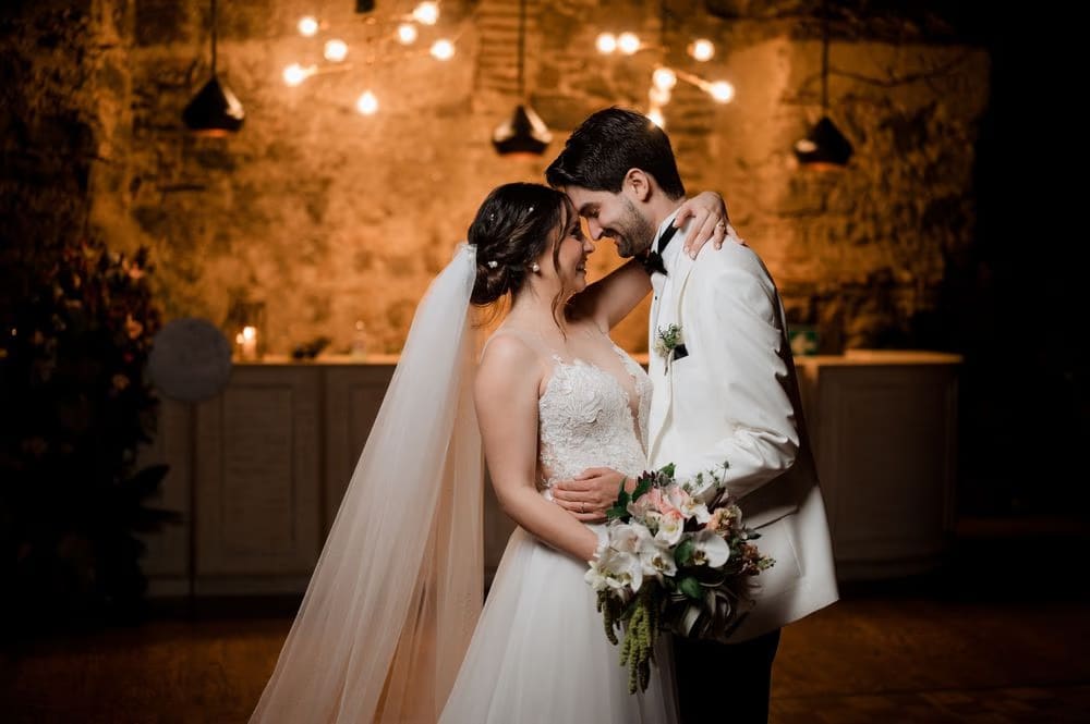 Bride and groom embrace foreheads under string lights in a candle-lit vault at the reception.