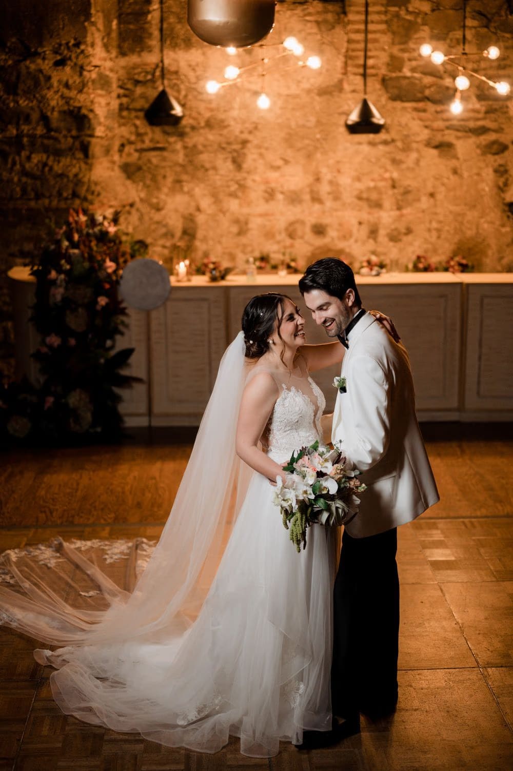 Couple share a quiet moment beneath the stone wall and copper pendant lights of the reception room.